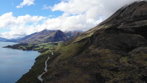 A ROAD BUILT ON THE FOOT OF A MOUNTAIN OVERSEEING THE LAKE