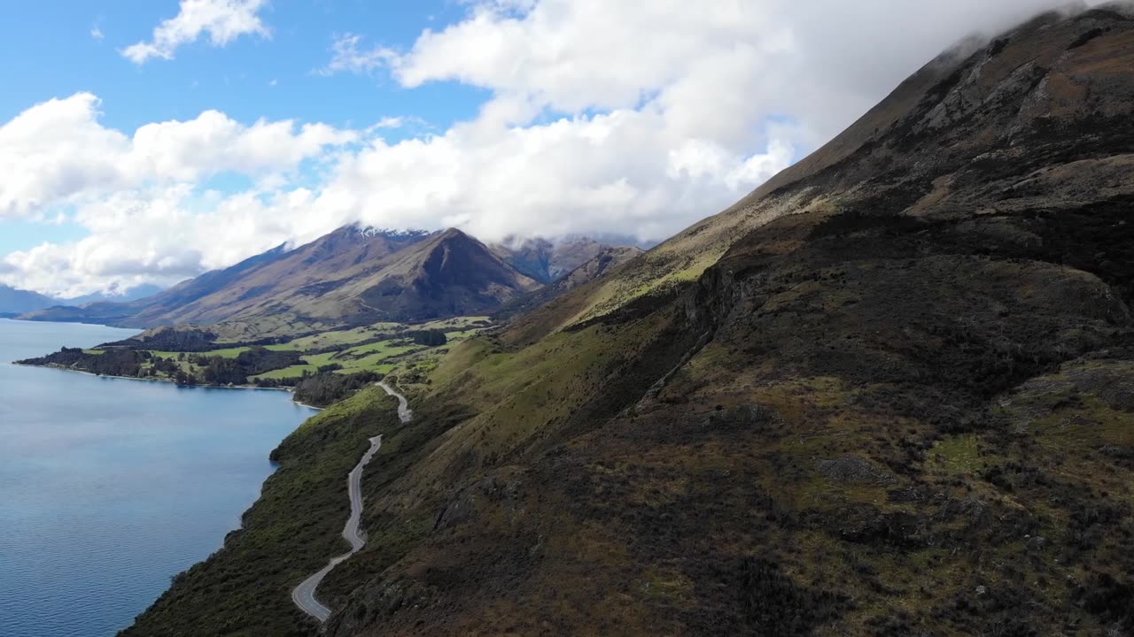A ROAD BUILT ON THE FOOT OF A MOUNTAIN OVERSEEING THE LAKE