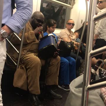 Guy in tan suit singing from blue speaker on subway