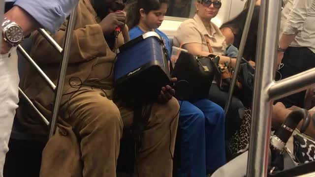 Guy in tan suit singing from blue speaker on subway