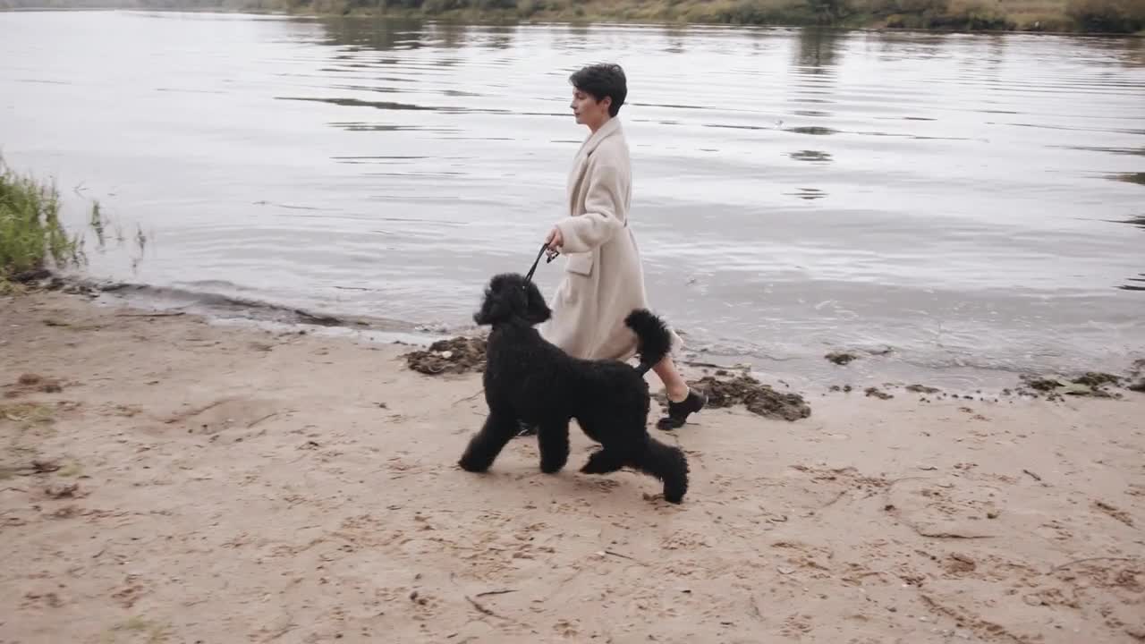 A charming young woman in a stylish white coat goes along the river bank