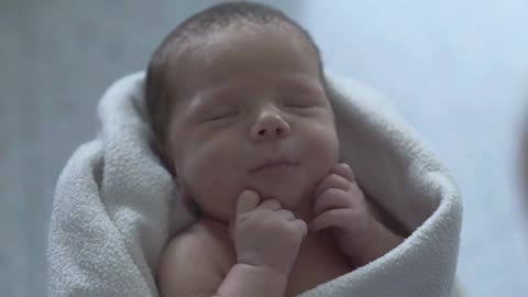 Adorable newborn baby sleeping in a blanket and holds his mother's hand