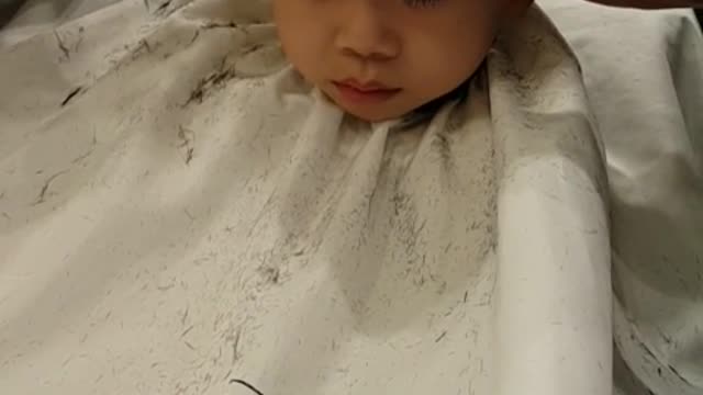 The baby is sleeping while having a haircut.