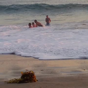 Several guys in the water keep getting knocked down by the waves