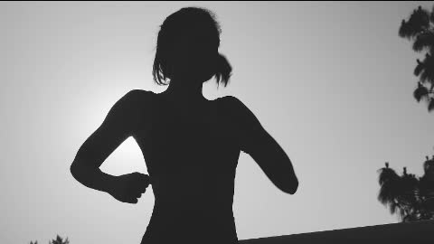 Silhouette of a young woman jogging in front of the sun