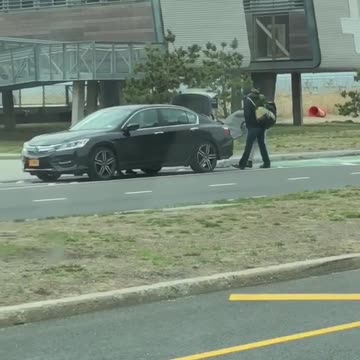 Two guys attempt to put surfboard in trunk of car