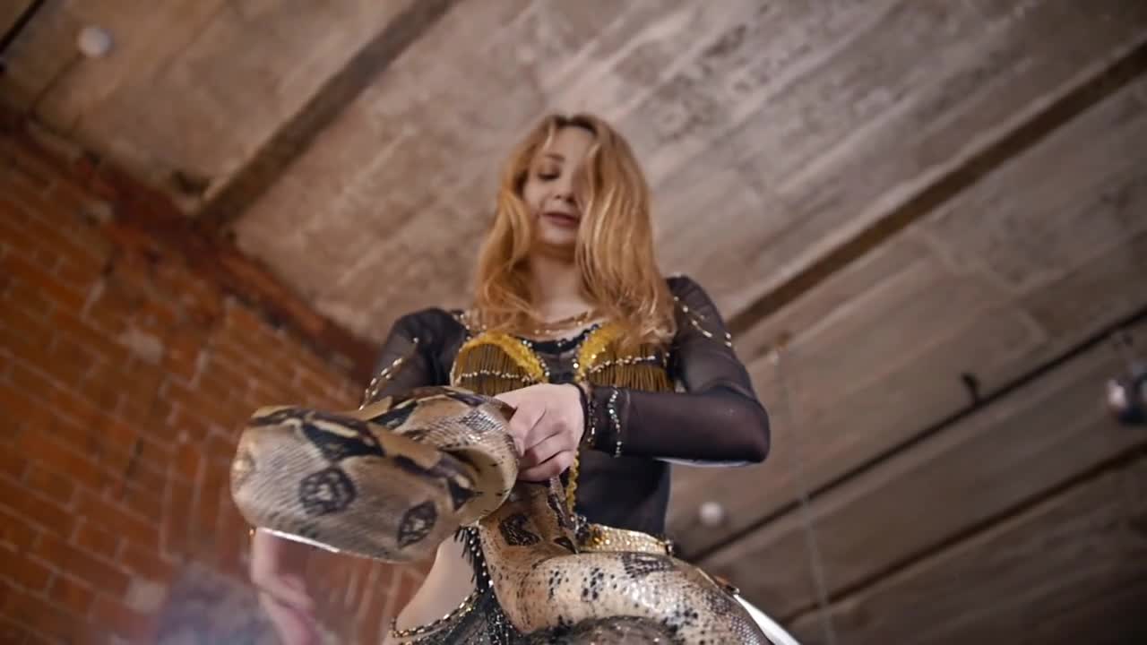 Attractive female circus actress dancing with python in a studio