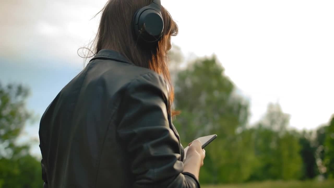 Girl, listening music from wi-fi headphones with a smartphone, walking in the park with her dog