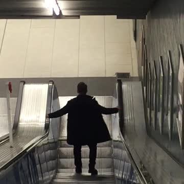 Jacket guy walking down escalator waves hands back and forth
