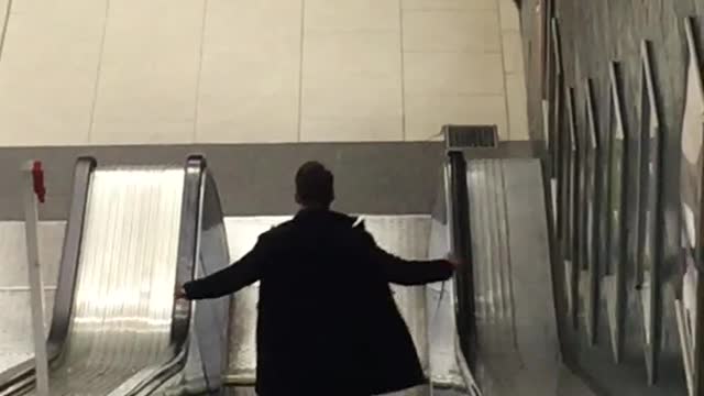 Jacket guy walking down escalator waves hands back and forth