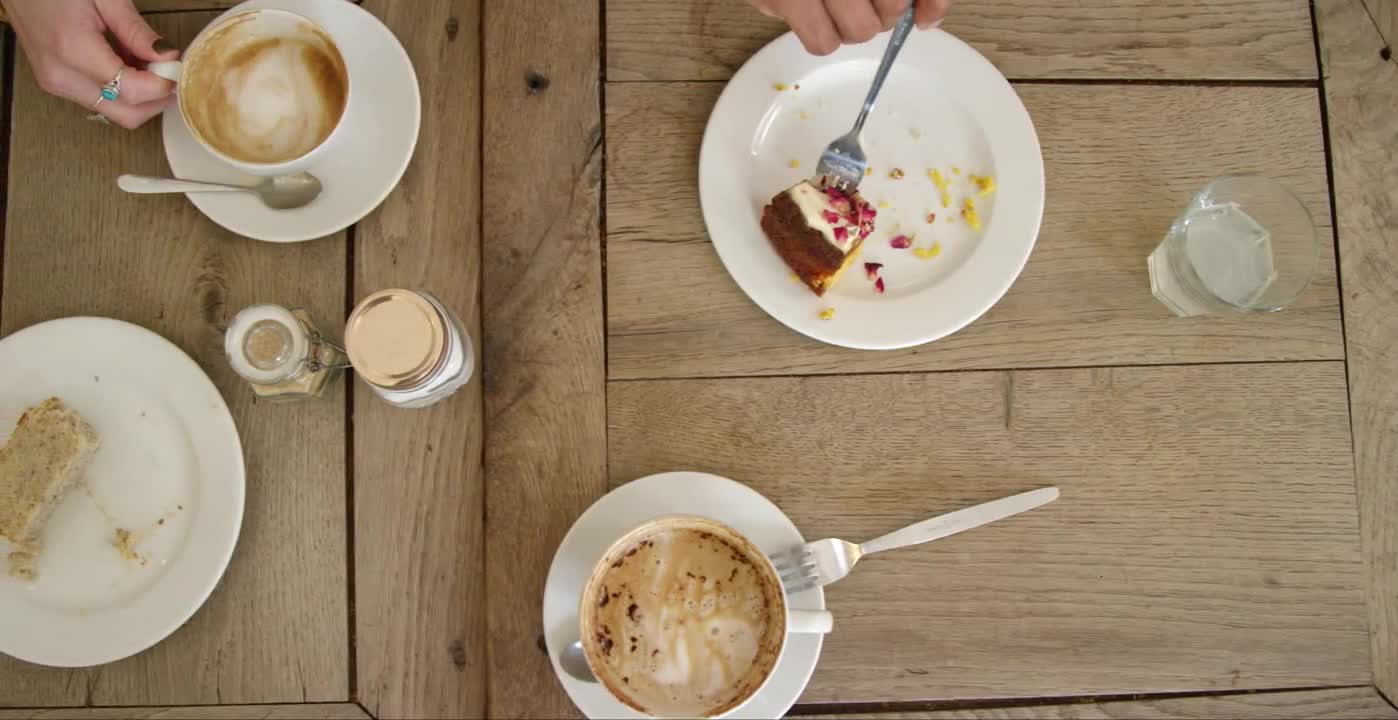 Overhead View Of Hands Lifting Coffee Mugs And Cake Off Cafe Table