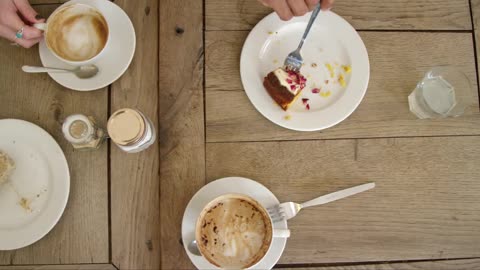 Overhead View Of Hands Lifting Coffee Mugs And Cake Off Cafe Table