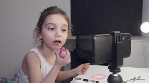 Little girl using lipstick and looking at the phone