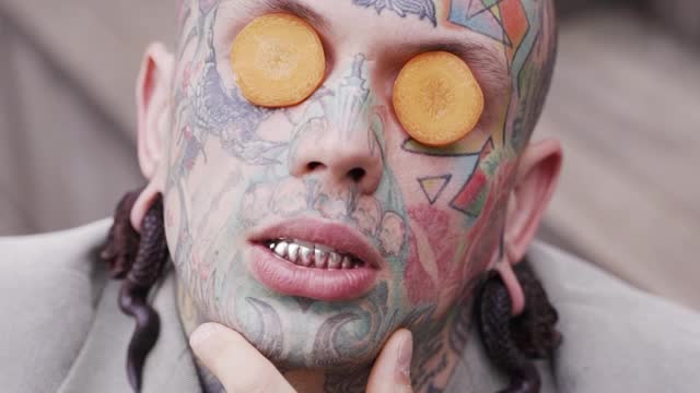 Tattooed Man Posing with Carrot Slices on Eyes