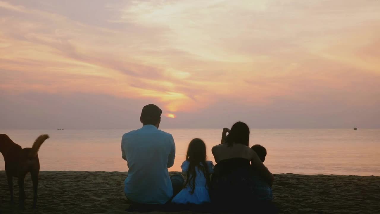 shot of happy family sit together watching amazing sunset on epic sea beach, two dogs playing by