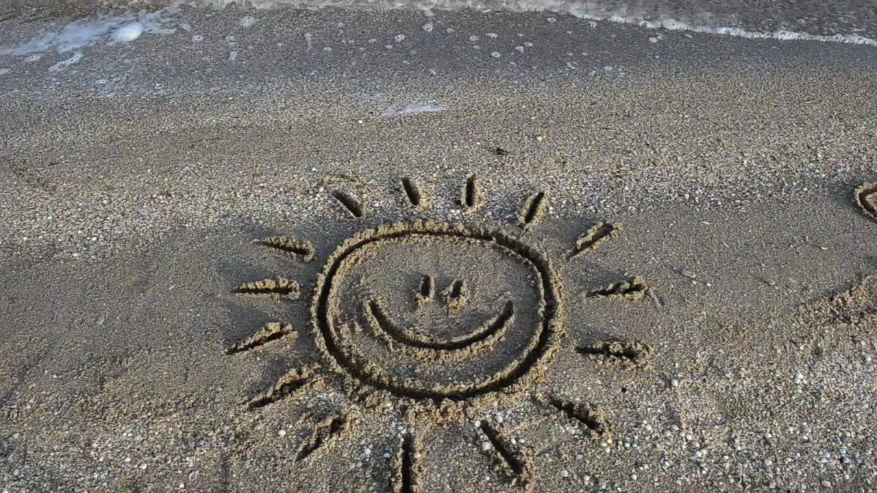 Smiling sun drawn in the sand on a beach