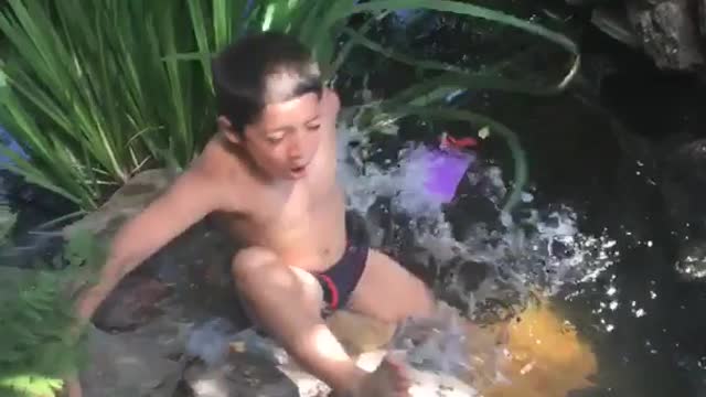 Shirtless kid standing on edge of pond falls into pond