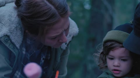 Little girl and her parents roasting marshmallows in a forest