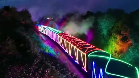 Steam train decked out in vibrant neon lights passes through countryside