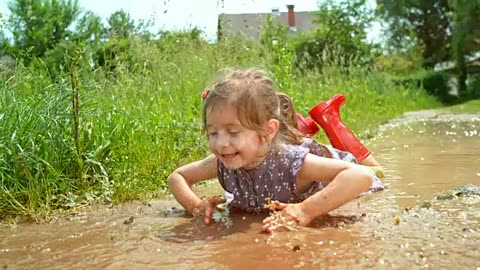 Slow motion wide handheld shot of a little girl in a dress and red rain boots