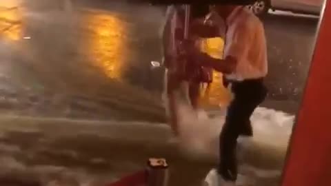 dude tries to help chick through the flooded road and she gets swept away