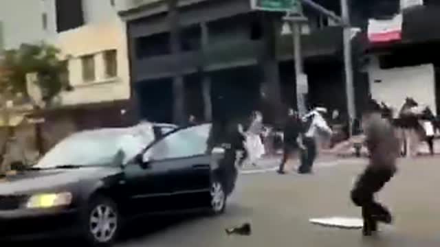 LA rioter lights firework on the street. Gets it thrown back into his car.