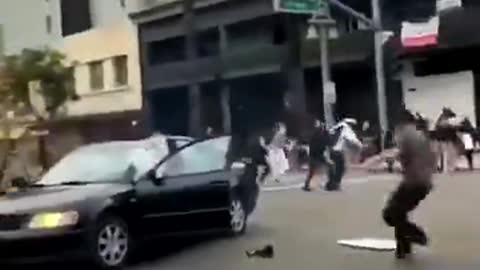 LA rioter lights firework on the street. Gets it thrown back into his car.