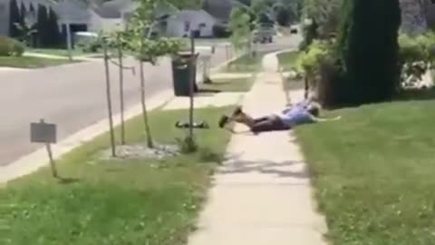 Man in blue falls off skateboard next to bush