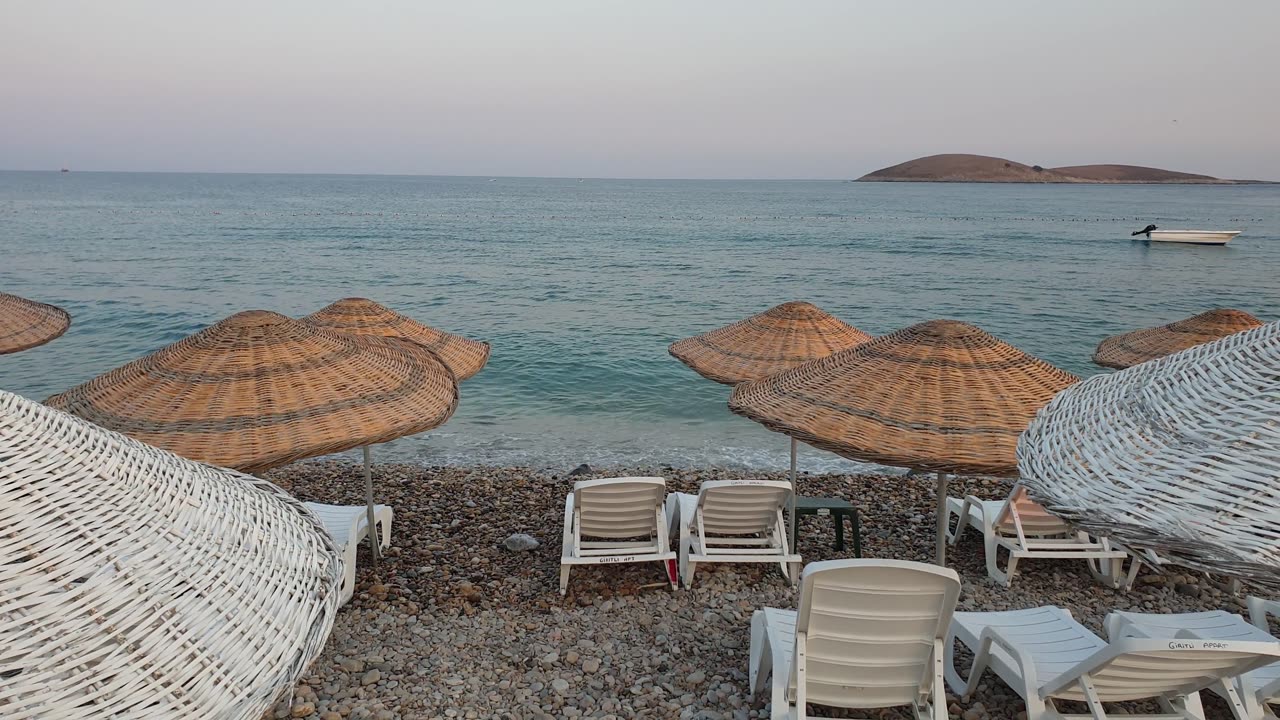 Lines Of Beach Chairs Shaded By Rattan Umbrellas On The Shore Of A Beach