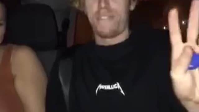 Blonde guy in black shirt with fiji water singing in car