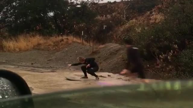 Guys trying to paddle and surf down muddy wet flooded street