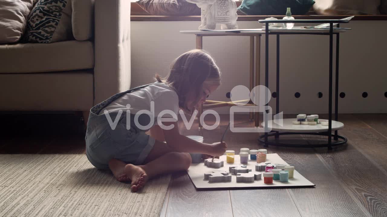 Side View Of A Blonde Girl Sitting On The Floor And Painting Animal Pieces