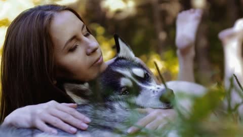 Close-up of attractive girl lying on grass hugging her husky dog and then looking at the camera