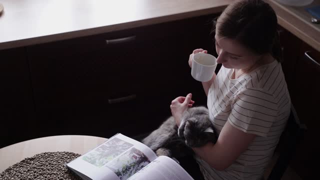 A Woman Petting a Cat While Reading a Book