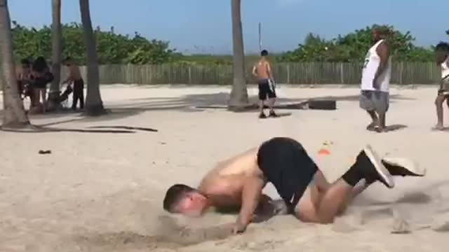 Shirtless man black shorts back flip fail in beach sand