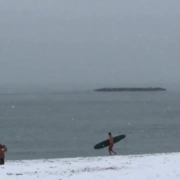 Guy gets ready to surf as its snowing at the beach