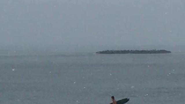 Guy gets ready to surf as its snowing at the beach