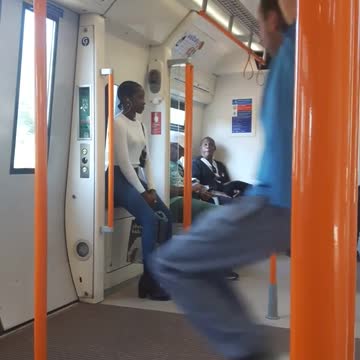 Man in blue swings from orange bars on train