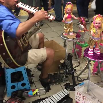 Guy playing piano flute with dolls dancing in front of him
