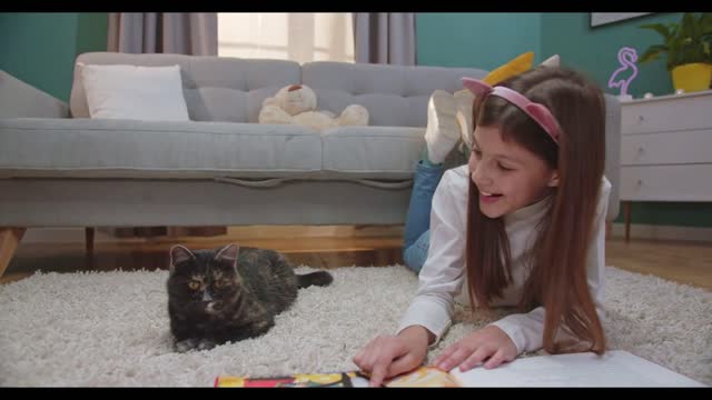 Cute Caucasian small girl in funny ears lying on floor and fliping pages of baby book