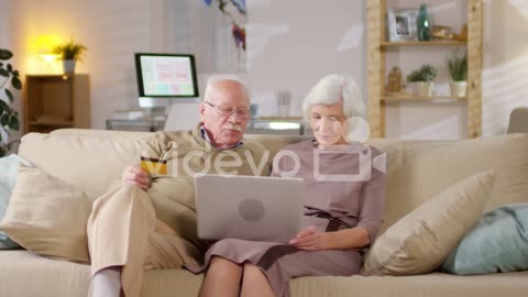 Retired Couple Sitting On Sofa At Home And Shopping Online Together 1