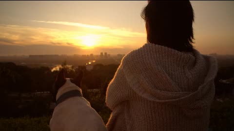 A woman with her dog watching the sunset