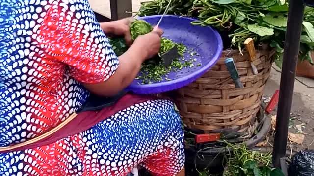 African Woman Cutting Fresh Pumpkin Leaves In The Market