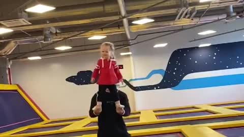 Dad Holds Toddler's Feet in Hands While Jumping on Trampoline in Jumping Park