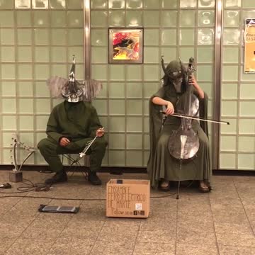 Two people in silver animal masks play instruments