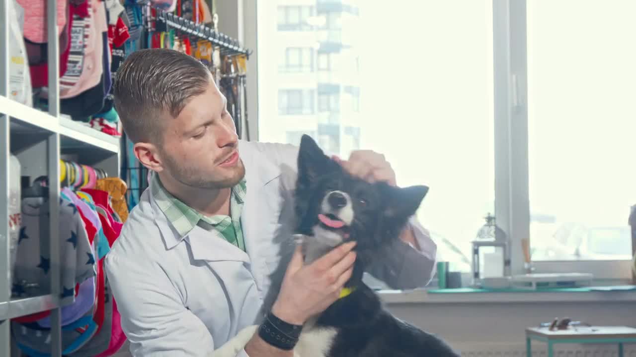 Handsome cheerful male veterinarian smiling to the camera, hugging adorable dog