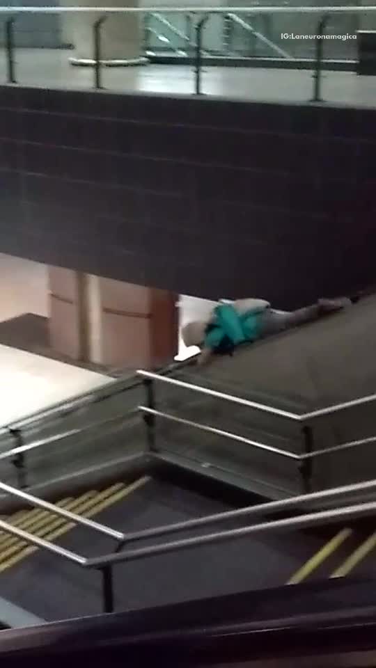 Blue jacket guy rides rail bannister of escalator