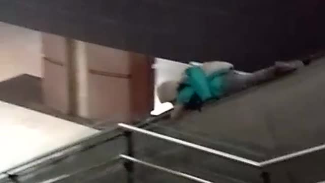 Blue jacket guy rides rail bannister of escalator