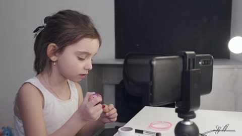 Little Girl Applying Lipstick While Looking At Her Smartphone