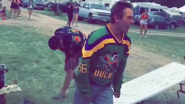 Man in green jersey does a flip gainer off of an rv onto a table